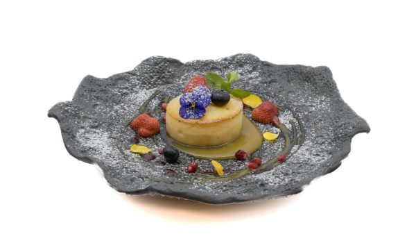 Assiette élégante présentant un gâteau basque garni de fruits frais sur fond blanc