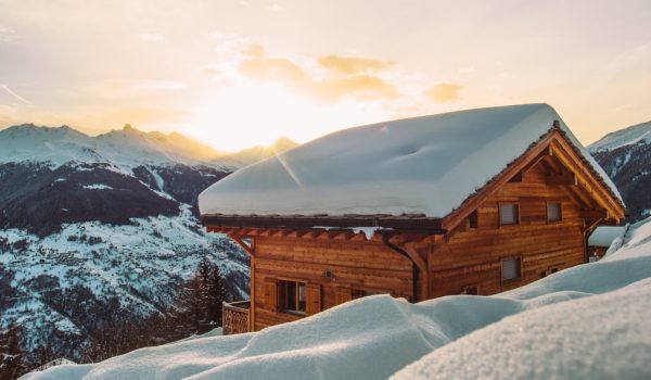 Coucher de soleil illuminant un chalet enneigé en montagne.