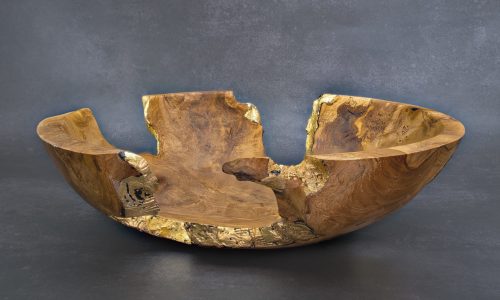 Photo d'une coupe en bois raffinée avec bordure dorée, présentée sur un fond texturé en béton ciré, mettant en valeur le mariage du rustique et du moderne.